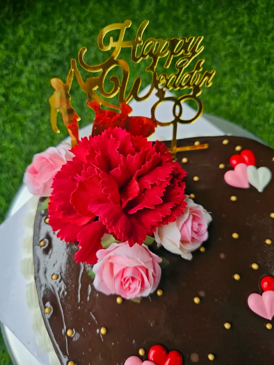 Chocolate celebration cake with fresh pink and red roses and anniversary hearts