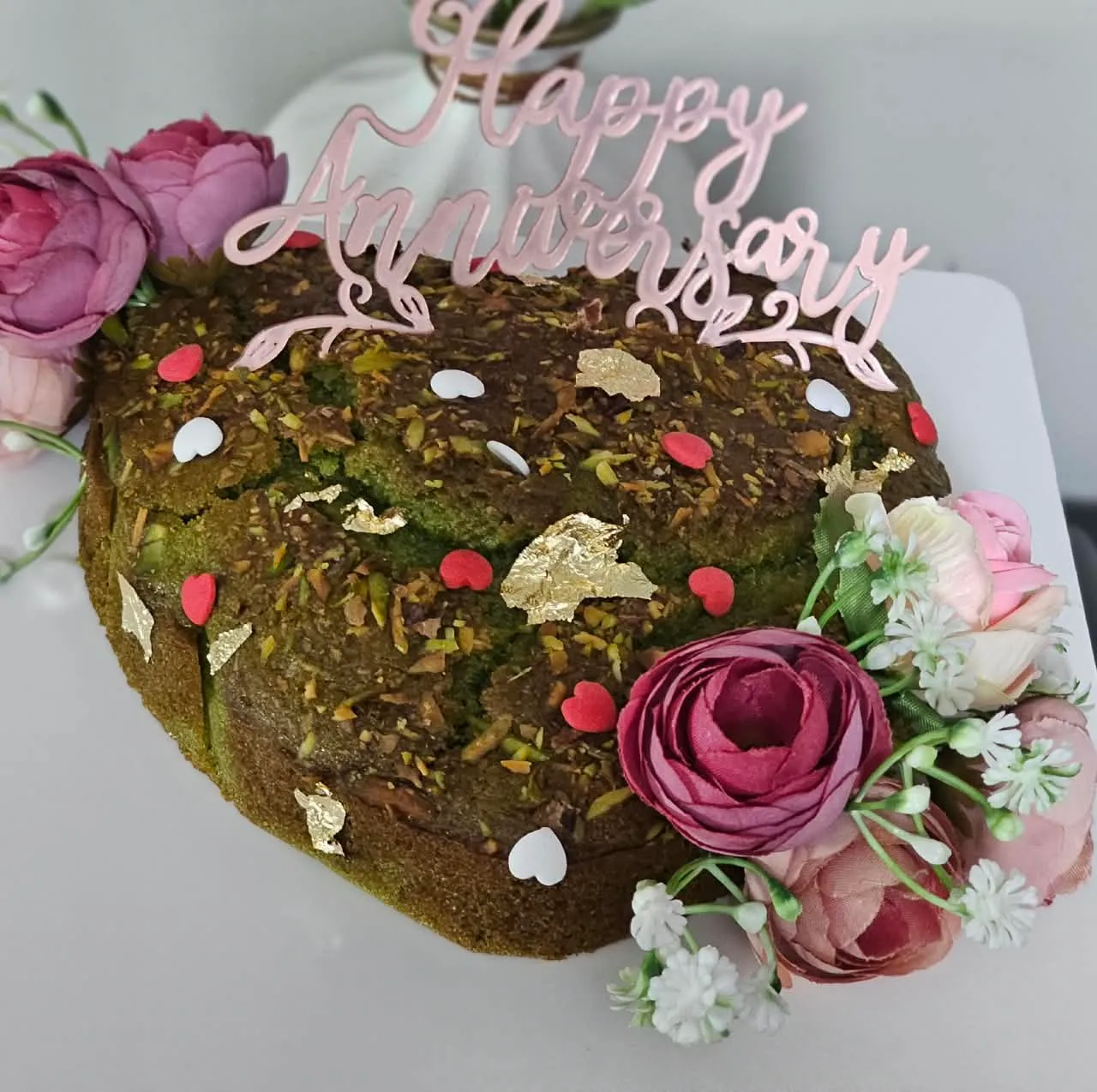 Handmade eggless pistachio anniversary heart cake topped with blush roses
