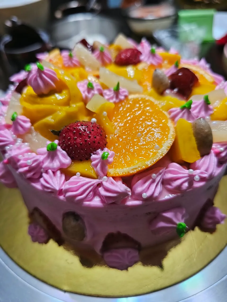 Pink-frosted cake with fresh oranges, strawberries and tropical fruits