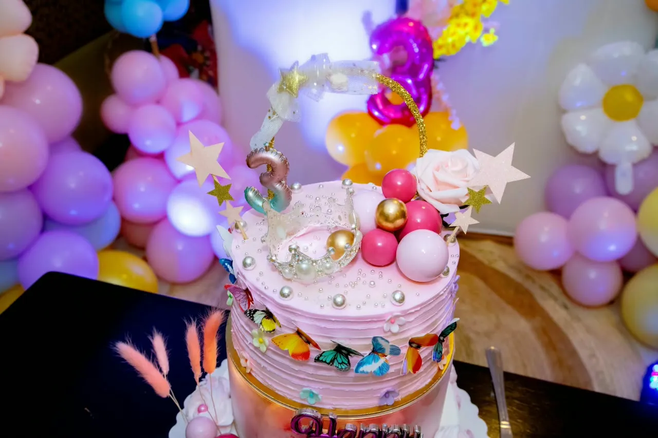 Pink tiered children’s cake with butterflies, pearl accents and crown topper